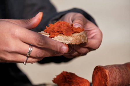 Téléchargez les photos : Personne méconnaissable dans le processus de propagation appétissant chorizo saucisse sur morceau de pain sur fond flou - en image libre de droit