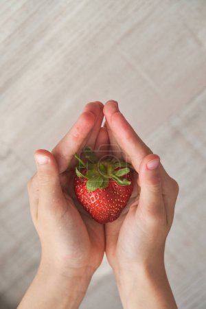 Téléchargez les photos : Vue du dessus de la récolte enfant anonyme montrant savoureuse fraise mûre dans les mains coupées sur fond flou - en image libre de droit