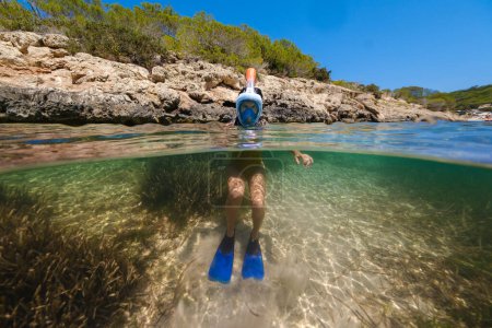 Foto de Niño irreconocible en máscara de buceo y aletas nadando en agua limpia de mar en la orilla del pueblo de Portinatx en Ibiza - Imagen libre de derechos