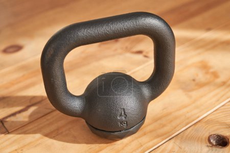 Photo for High angle of professional heavy cast iron four kilogram kettlebell placed on wooden floor and lit by sun rays - Royalty Free Image