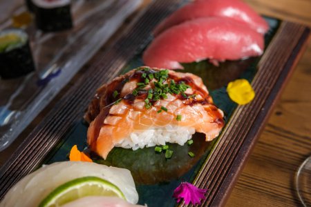 Photo for From above of appetizing Japanese sushi with raw salmon and chopped green onion on plate with flower petals - Royalty Free Image