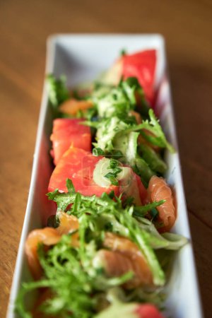 Téléchargez les photos : Photo verticale de saumon mariné avec salade d'escarole et sauce moutarde servie dans une assiette rectangulaire en céramique blanche sur une surface en bois - en image libre de droit
