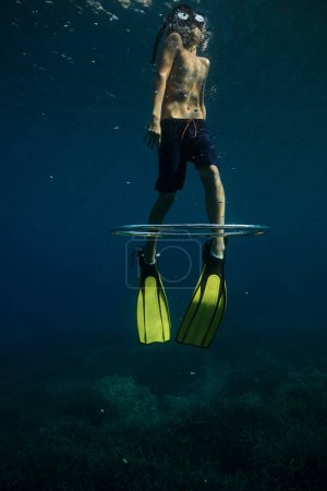 Téléchargez les photos : De dessous de plongeur torse nu méconnaissable en palmes et masque de plongée en apnée montant avec anneau à bulles pendant les vacances - en image libre de droit