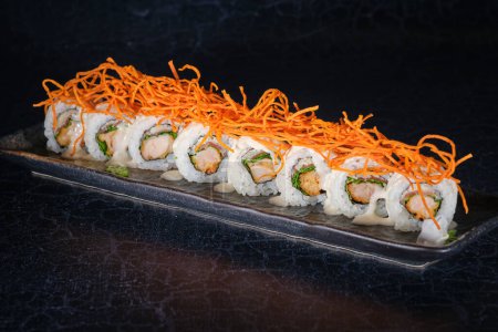 Téléchargez les photos : Rangée de sushi maki au saumon décoré de carotte râpée servie sur une assiette de marbre posée sur une table noire - en image libre de droit