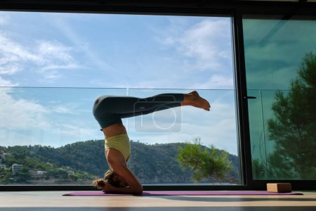 Téléchargez les photos : Vue de côté niveau du sol de la femelle tranquille en vêtements de sport équilibrage sur le tapis à Urdhva Dandasana tout en faisant du yoga sur la terrasse par une journée ensoleillée - en image libre de droit