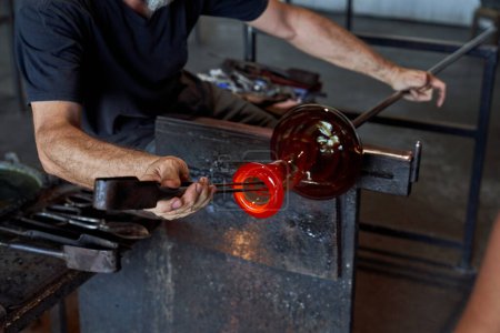 Photo for Crop anonymous male master using professional metal tool to shape incandescent glass vase while working in manufactory - Royalty Free Image