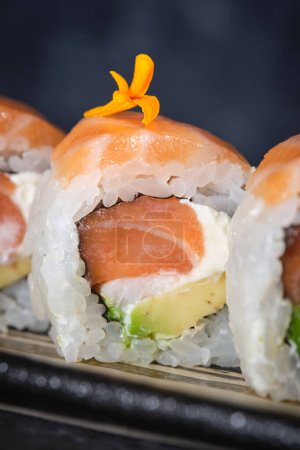 Foto de Primer plano de la fila de rollos frescos de sushi de California con salmón servido en el plato sobre fondo oscuro - Imagen libre de derechos
