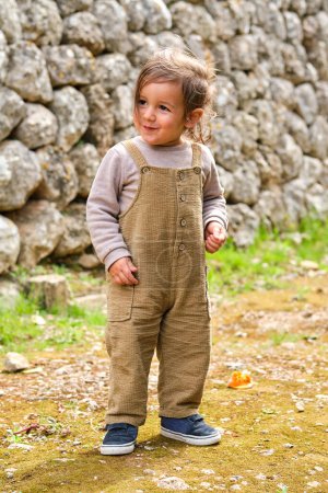 Foto de Niño sonriente con ropa casual mirando hacia otro lado en terreno seco contra la pared de piedra durante el día - Imagen libre de derechos