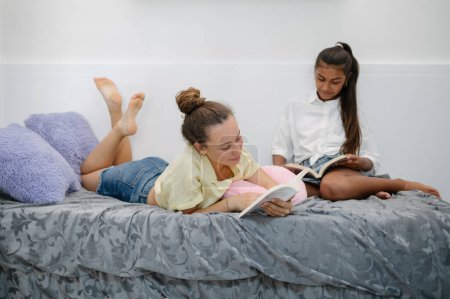 Téléchargez les photos : Corps complet de diverses copines adolescentes allongées sur le lit et lisant des livres ensemble - en image libre de droit