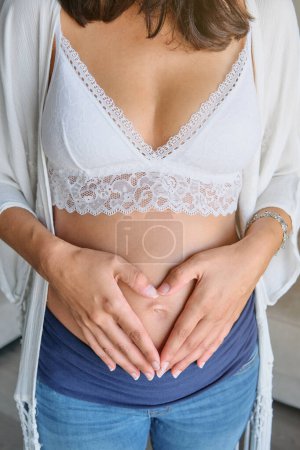 Photo for Unrecognizable crop expecting female in white lace bra and jeans embracing tummy with tenderness - Royalty Free Image