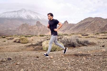 Téléchargez les photos : Full body side view of male traveler in t-shirt running on rocky terrain near volcanic mountain Teide in daylight in Tenerife Îles Canaries Espagne - en image libre de droit