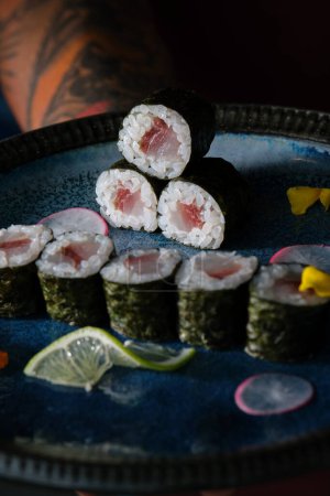 Photo for From above of crop anonymous waiter with delicious sushi rolls with salmon on tray with flowers and slices of lemon against blurred background - Royalty Free Image