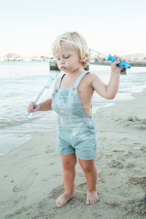 Téléchargez les photos : Corps complet d'adorable petit enfant jouissant d'un jouet à bulles sur une plage de sable lavée par la mer calme en station balnéaire - en image libre de droit