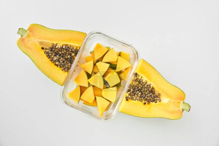 Foto de Vista superior de la pila de cubos maduros de papaya colocados en un recipiente de vidrio entre la mitad de la fruta sobre fondo blanco - Imagen libre de derechos