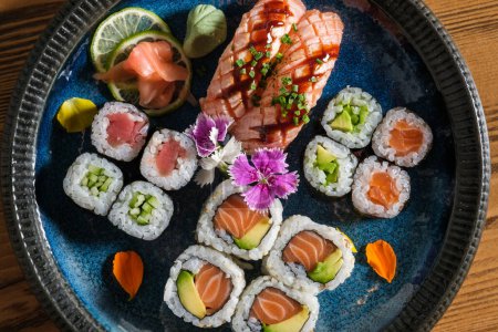 Photo for Top view of delicious assorted sushi rolls with raw salmon on plate with ginger wasabi and slices of lime on wooden table - Royalty Free Image