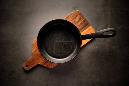 Photo for Top view of empty metal pan placed on wooden cutting board on marble table against gray background - Royalty Free Image