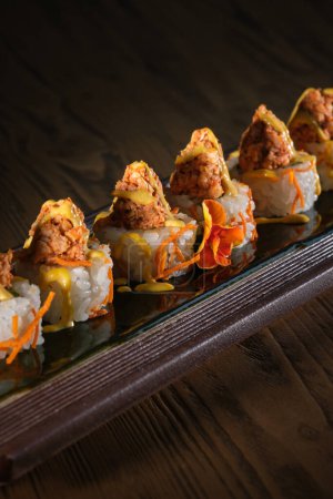 Téléchargez les photos : Du dessus des sushis appétissants garnis de saumon et de sauce fraîche servis sur un plateau en bois sur la table du restaurant sur fond noir - en image libre de droit