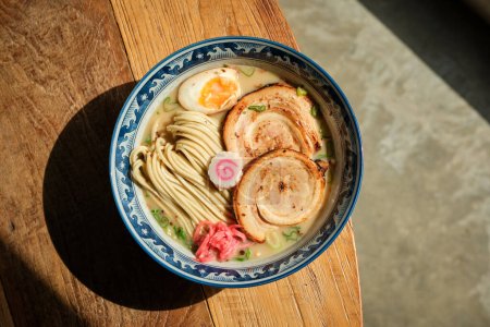 Top view of bowl with delicious ramen placed on edge of sunlit table during lunch in Japanese restaurant