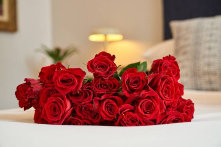 Photo for Bunch of fresh lush roses with red tender petals placed on bed in blurred cozy room at hotel - Royalty Free Image