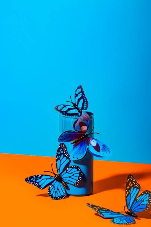Téléchargez les photos : Papillons en plastique fragiles attachés sur bouteille boîte bleue sur fond coloré - en image libre de droit