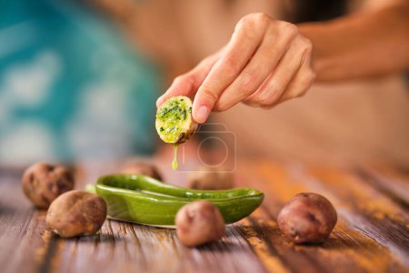 Téléchargez les photos : Une femelle méconnaissable trempant la moitié d'une petite pomme de terre bouillie dans une sauce mojo de coriandre pendant le déjeuner - en image libre de droit