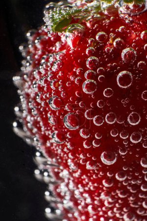 Téléchargez les photos : Gros plan fraise rouge fraîche recouverte de bulles transparentes de dioxyde de carbone sur fond noir - en image libre de droit