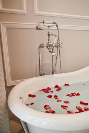 Photo for Interior of bathtub with water covered with rose petals and vintage faucet located in hotel suite - Royalty Free Image