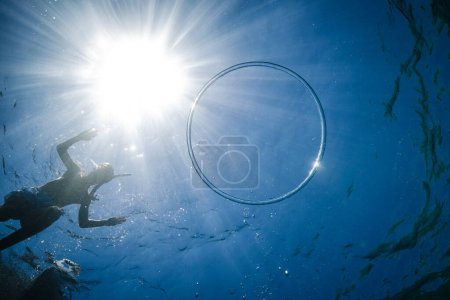 Photo for From below view from water of anonymous kid in snorkeling mask jumping into blue sea with ring bubble under bright sun rays - Royalty Free Image