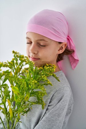 Photo for Side view of calm boy in pink bandana with goldenrods closing eyes on white background - Royalty Free Image