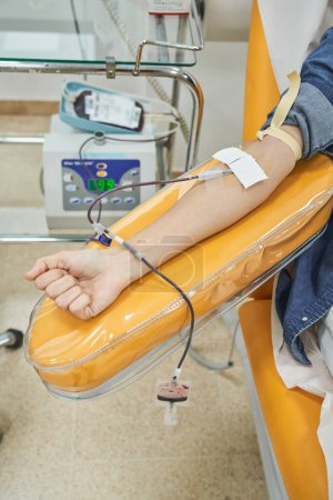 Téléchargez les photos : De dessus de la culture femme anonyme assis sur le lit de thérapie et donnant du sang avec mélangeur de sang donneur en laboratoire en clinique - en image libre de droit