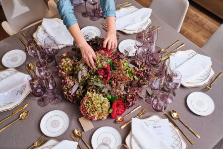 Téléchargez les photos : De dessus de la récolte fleuriste femelle anonyme organiser fleurs fleuries assorties sur table de banquet avec vaisselle et couverts servis - en image libre de droit
