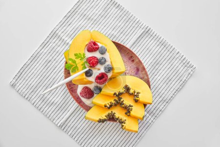 Téléchargez les photos : Vue du dessus du délicieux dessert à la papaye avec des framboises au yaourt et des bleuets servis sur une assiette en céramique rose avec une cuillère et placés sur une serviette - en image libre de droit
