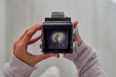 Photo for Crop unrecognizable person showing photography of child on vintage camera screen on light background - Royalty Free Image