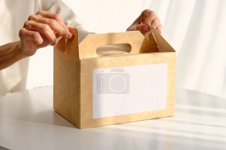 Téléchargez les photos : Crop anonyme femelle avec boîte en carton avec commande placée sur la table blanche au soleil - en image libre de droit