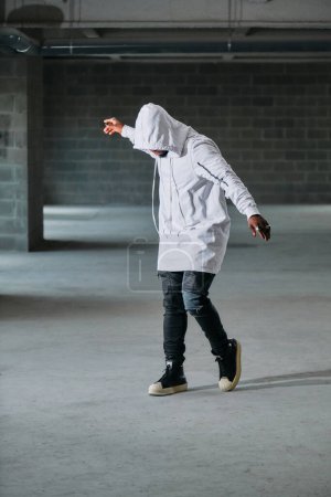 Photo for Full length of mysterious male model with face hidden under hood dancing in underground parking lot - Royalty Free Image