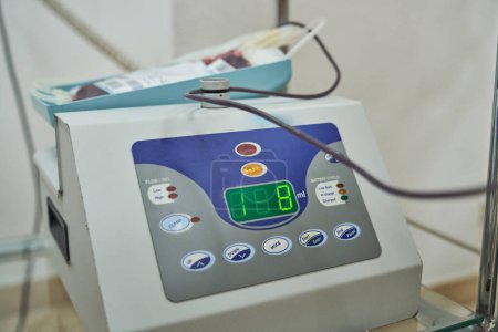 Foto de Moderna máquina de monitoreo de recolección de sangre colocada en estante de vidrio en laboratorio en el hospital midiendo el peso de la bolsa con sangre - Imagen libre de derechos
