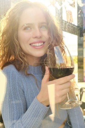 Photo for Portrait of beautiful positive young curly haired woman with glass of red wine looking at camera - Royalty Free Image