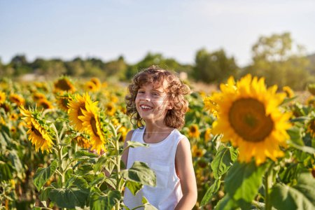 Photo for Portrait of smiling preteen male in white dress looking at camera while standing amidst sunflower plants in countryside - Royalty Free Image