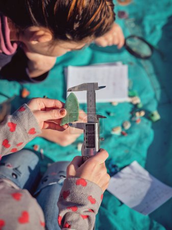 Photo for Top view of crop anonymous preteen girl putting piece of picked waste plastic into metal digital caliper while measuring assorted garbage - Royalty Free Image