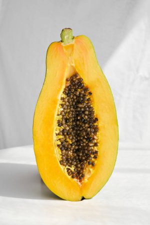 Téléchargez les photos : Fruits de papaye mûrs tropicaux coupés en deux avec des graines et de la pulpe brillante placés sur la table avec ombre au soleil en studio - en image libre de droit