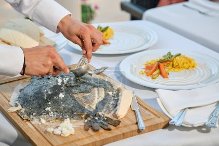 Téléchargez les photos : Personne anonyme en train de préparer un plat de poisson à l'aide d'une fourchette et d'une cuillère, debout à table avec une nappe blanche et travaillant dans un restaurant - en image libre de droit