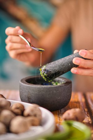 Photo for Soft focus of crop female adding spoonful of olive oil to mortar with mojo de cilantro sauce while cooking papas de Tenerife dish for lunch - Royalty Free Image