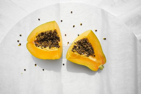 Téléchargez les photos : Vue de dessus de papaye bio fraîche coupée en morceaux et placée sur une table en bois gris avec des graines éparpillées autour - en image libre de droit
