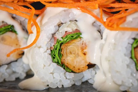 Téléchargez les photos : Gros plan de délicieux sushi maki au saumon décoré de carotte râpée et sauce servie dans une assiette - en image libre de droit