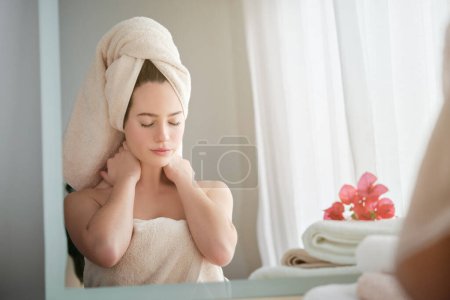 Téléchargez les photos : Charmante femelle avec des cheveux enveloppés dans une serviette blanche assise à une table en bois et rêvant après avoir fait la routine beauté du matin à la maison - en image libre de droit