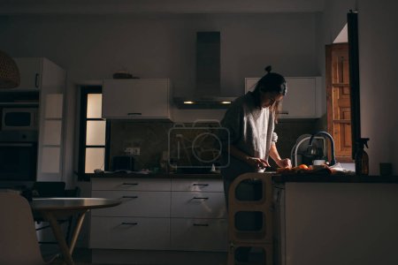 Foto de Vista lateral de ama de casa cortando frutas mientras se prepara un desayuno saludable en la cocina con muebles blancos - Imagen libre de derechos