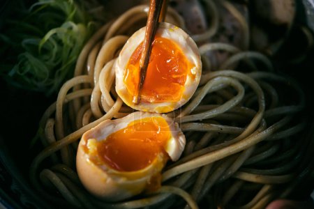 Photo for High angle of delicious ramen with halves of juicy chicken egg between food sticks on cooked noodles for lunch - Royalty Free Image