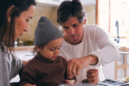 Téléchargez les photos : Cultiver mère et père saler oeuf bouilli de fille à table dans la cuisine sur fond flou - en image libre de droit