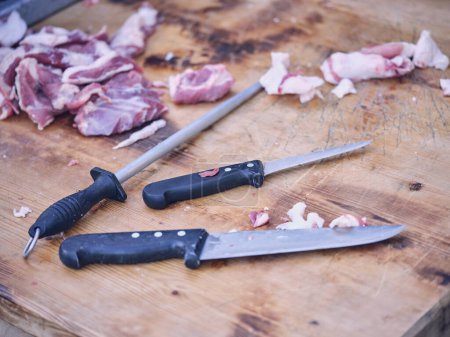 Foto de De arriba del juego del equipo agudo para el carnicero, que consiste de los cuchillos y el toldo, colocado en la tabla de cortar de madera cerca de los pedazos de la carne en el taller - Imagen libre de derechos