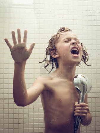 Photo for Cheerful shirtless child raising arm and singing in light tiled bathroom with shower head in hand as microphone - Royalty Free Image